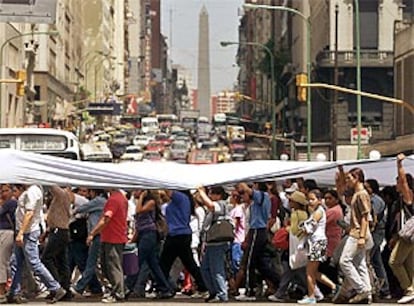 Cientos de parados recorren en una manifestación el centro de Buenos Aires bajo una inmensa bandera argentina.