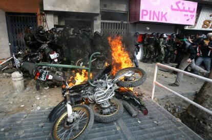 Manifestantes de la oposición tiran piedras a agentes de policía acorralados en Teherán, mientras arden varias motos de las fuerzas de seguridad.