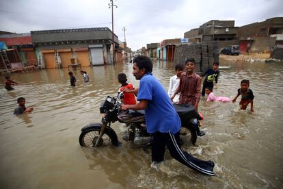 Hombre y niños se abren paso a través de un camino inundado por las fuertes lluvias monzónicas en Karachi (Pakistán). Al menos doce personas perdieron la vida electrocutados cuando las fuertes lluvias azotaron Karachi y otras partes de Sindh.