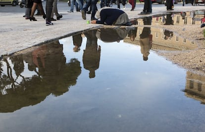 Una mujer pidiendo limosna se refleja en un charco, en el centro de Roma.