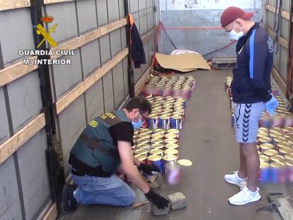 Un agente abre latas de tomate llenas de hachís ante la mirada de un narcotraficante.
