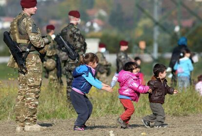 Crianças brincam perto da fronteira eslovena vigiadas por soldados perto de Rigonce, Eslovênia, em 26 de outubro.