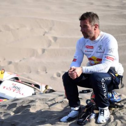 Loeb, sentado junto a su Peugeot a la espera de ayuda.