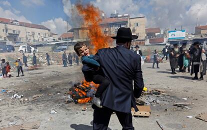 Un judío ultraortodoxo sostiene a un niño cerca de una hoguera donde se queman elementos fermentados durante el ritual de Biur Chametz, el 19 de abril de 2019.