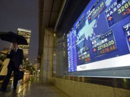 Un peatón camina junto a una pantalla informativa en la que aparece información bursátil en Tokio (Japón). EFE/Archivo