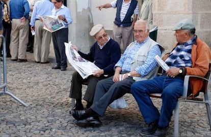 Aposentados portugueses leem jornais em uma rua.