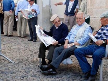 Aposentados portugueses leem jornais em uma rua.