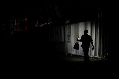 Un venezonalo usa la linterna del teléfono para alumbrarse mientras camina por una calle de Caracas, durante un corte eléctrico. 