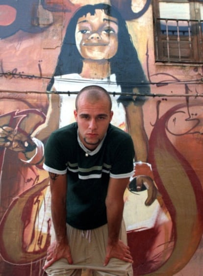 'El Niño de las Pinturas' posa junto a una fachada en Granada con sus grafitis.