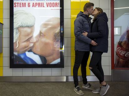Una pareja se besa junto a un poster con una caricatura en la que el pol&iacute;tico holand&eacute;s Geert Wilders besa al presidente ruso Vald&iacute;mir Putin en el metro de &Aacute;msterdam.