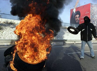 Un seguidor de Hezbolá quema neumáticos en frente de un póster del líder del movimiento, Hasán Nasraláh. La carretera del aeropuerto permanece cerrada desde primera hora de la mañana.