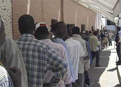 Colas de inmigrantes, vigilados por la policía, en los comedores de la Cruz Blanca en Ceuta.