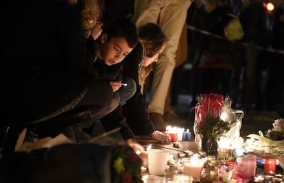 Un grupo de personas, entre ellas un niño, colocan flores y velas cerca de la sala Bataclan, de París, uno de los escenarios de los ataques yihadistas cometidos en la noche del 13 de noviembre de 2015.