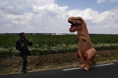 Un fotógrafo toma fotos de un espectador vestido con un disfraz de dinosaurio, en la ruta de la octava etapa de la 105ª edición de la carrera ciclista Tour de France, entre Dreux y Amiens, en el norte de Francia, el 14 de julio de 2018.