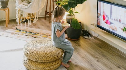 Una niña come delante de la televisión.