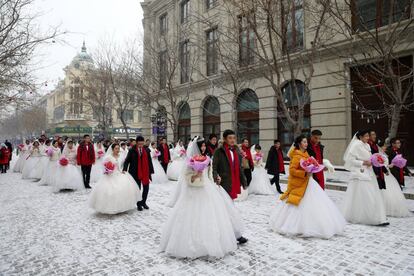 Las parejas recién casadas chinas desfilan en el centro de la calle durante una ceremonia de boda colectiva en el 34º festival internacional de esculturas de hielo y nieve de Harbin, en Harbin (China).