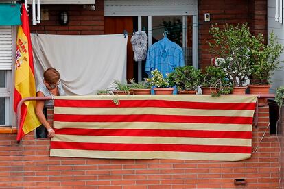 Una mujer coloca la bandera catalana en un balcón de Barcelona vecino a otro del que cuelga la de España.
