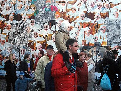 Turistas en el carnaval de Binche, en Bélgica, con los </i>Gilles,</i> los personajes característicos de la celebración, representados en la pared.