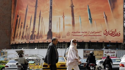 Peatones en Teherán pasan junto a una valla publicitaria con imágenes de misiles iraníes y una frase que reza en persa "Israel es más débil que la araña doméstica".