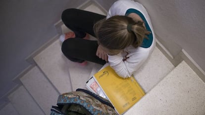 Una menor, en una escalera con los cuadernos y libros de clase. 