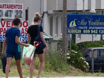 Tres personas caminan junto a varios carteles de viviendas en venta y en alquiler en A Mariña (Lugo)