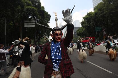 Un hombre con máscara de diablo baila, con el Ángel de la Independencia a sus espaldas.