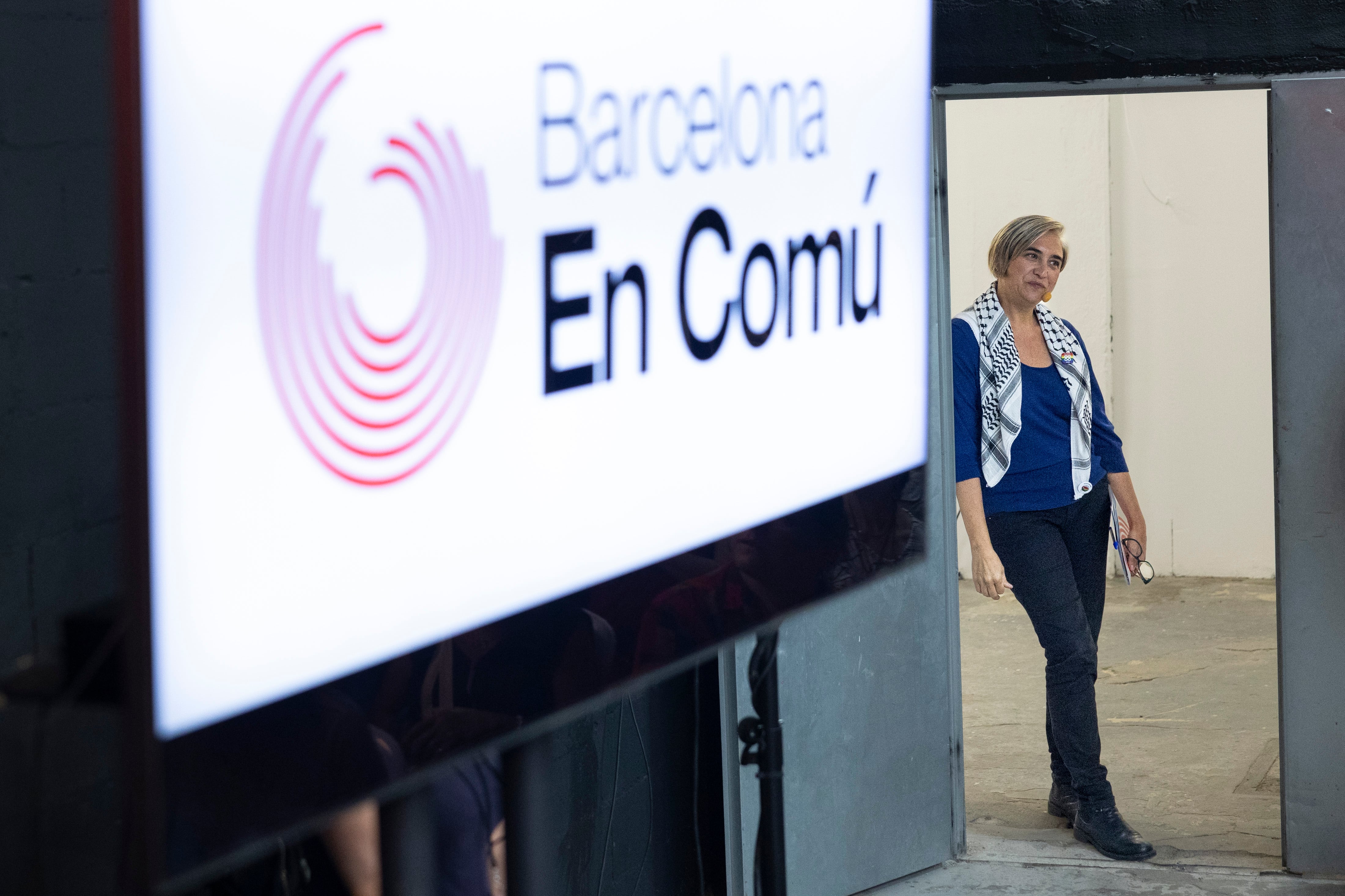 Ada Colau en Barcelona en 2024. En primer término, un cartel de Barcelona en Comú.