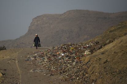 Un niño lleva bolsas de supermercado mientras camina por una carretera en una colina en Kabul.