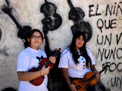 Agustina Llopis y Paloma Tapia frente a un mural de la plaza con una leyenda que da sentido al proyecto: "El niño que toca un violín nunca va a tocar un arma".