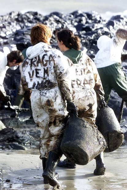 Voluntarios trabajan en la limpieza de la segunda marea negra llegada a la playa de Nemiña, el 1 de diciembre de 2002, en Laxe (A Coruña). En la espalda de los el mono de las jóvenes, pueden leerse las frases "Fraga ven" y "¿Donde está Fraga?", en referencia a la ausencia del presidente de la Xunta de Galicia en los lugares de la catástrofe.