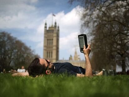Un hombre lee un libro electrónico en un parque de Londres.