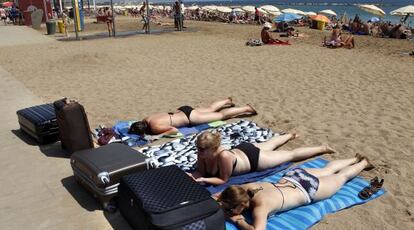 Tres turistas tomando el sol en la playa de la Barceloneta.