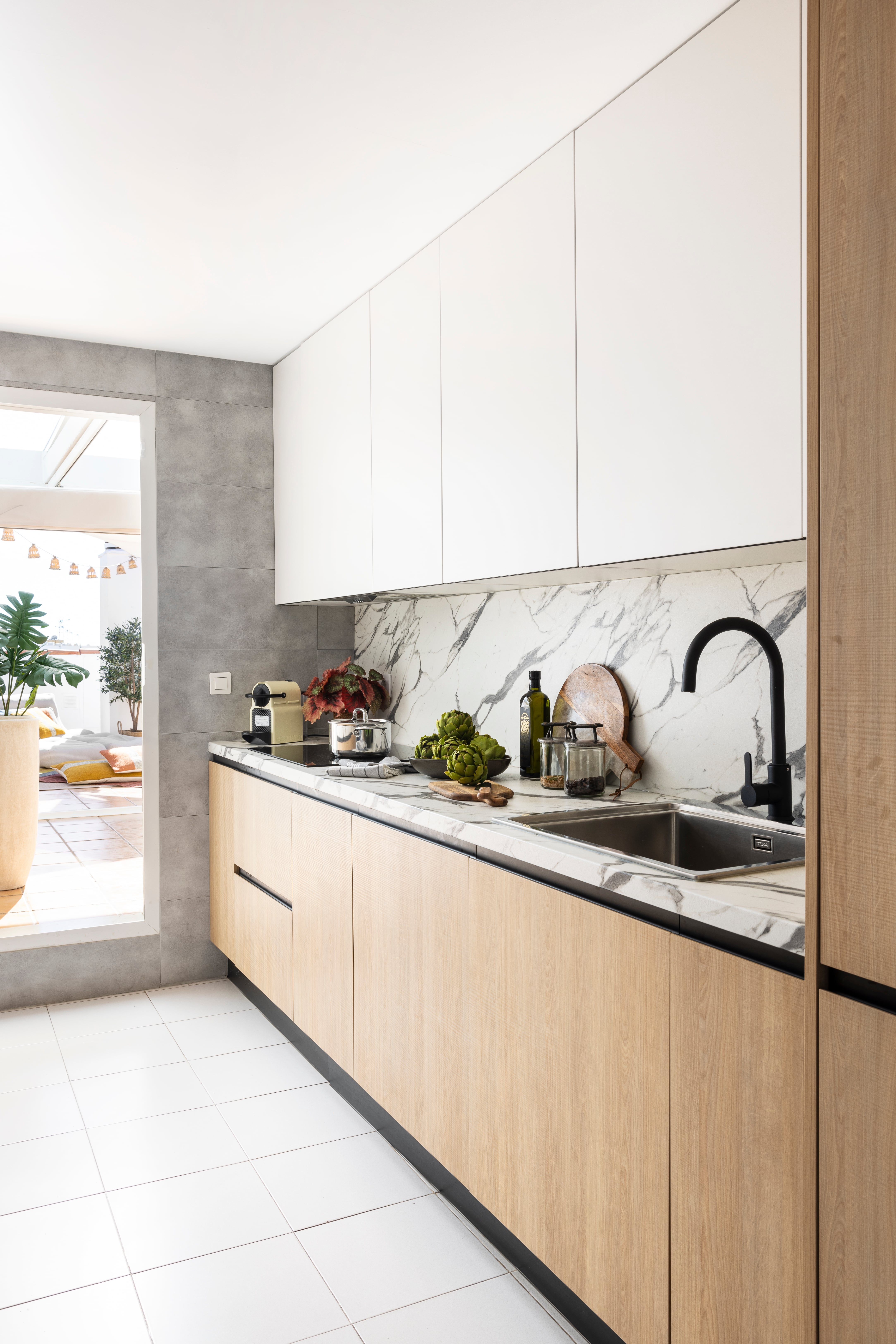 Revestimientos vinílicos que simulan el  mármol en la encimera y el salpicadero, y un vinilo de efecto porcelánico gris en la pared lateral son algunos de trampantojos de esta cocina diseñada por Alberto Torres. 