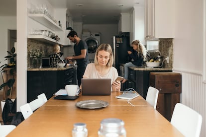 Una mujer teletrabaja mientras su pareja cocina y atiende a sus hijos.