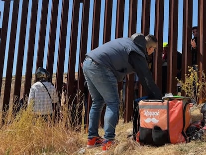 Un repartidor de comida entrega alimentos a migrates que esperan del otro lado del muro fronterizo en Tijuana, México, el 10 de mayo 2023.