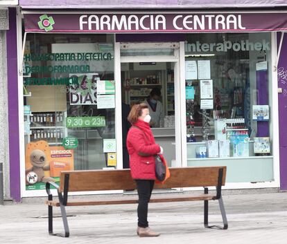 Una mujer protegida con mascarilla al lado de una farmacia abierta durante el estado de alarma.
