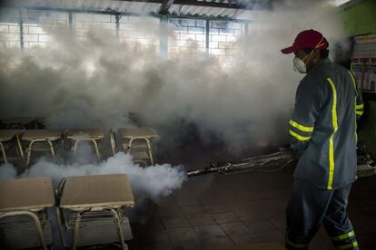 Un trabajador fumiga el salón de una escuela en El Salvador.