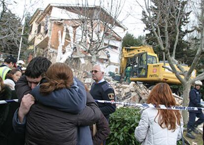Dos familiares del hombre fallecido en la explosión de San Lorenzo de El Escorial se abrazan ante los escombros en los que quedó convertido el chalé.