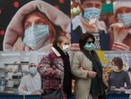 Two women wearing face masks to protect against the spread of coronavirus, walk past posters in the street in Madrid, Spain, Thursday, Dec. 17, 2020. Some of Spain's regions are tightening health restrictions for the Christmas holidays with new COVID-19 cases already on the rise again. (AP Photo/Paul White)