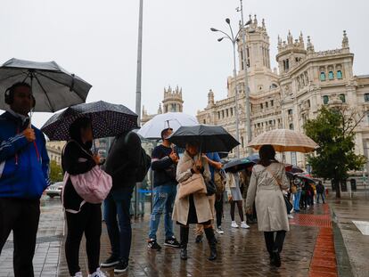 Varias personas se protegen del diluvio frente al Palacio de Cibeles, este jueves en Madrid.