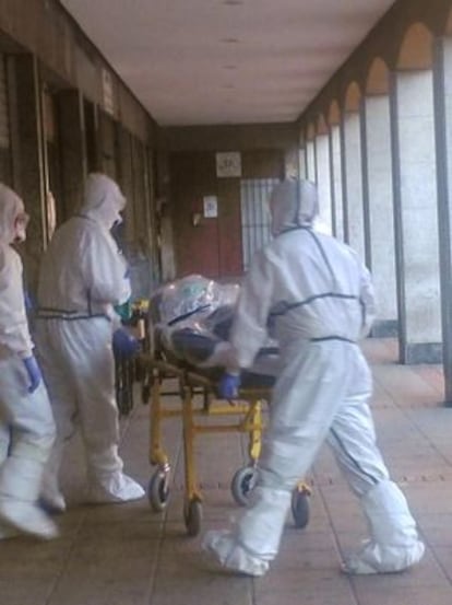 Personal sanitario, equipado con mascarillas y buzos, traslada al paciente desde su domicilio.