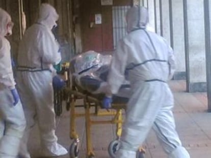 Personal sanitario, equipado con mascarillas y buzos, traslada al paciente desde su domicilio.