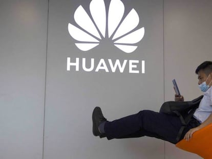 Un hombre consulta su móvil junto a un logo de Huawei. 