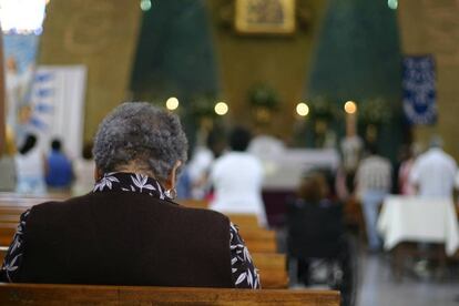 Una mujer reza sentada en un banco de una Iglesia católica.