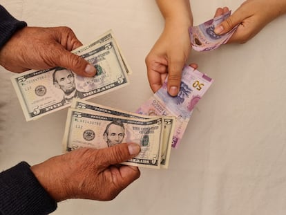 Dos personas intercambian billetes de dólares por pesos mexicanos.