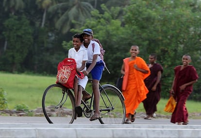 Unos niños adelantan con su bici a unos monjes budistas a la salida de la escuela en Piliyandala, en un barrio de Colombo en Sri Lanka.