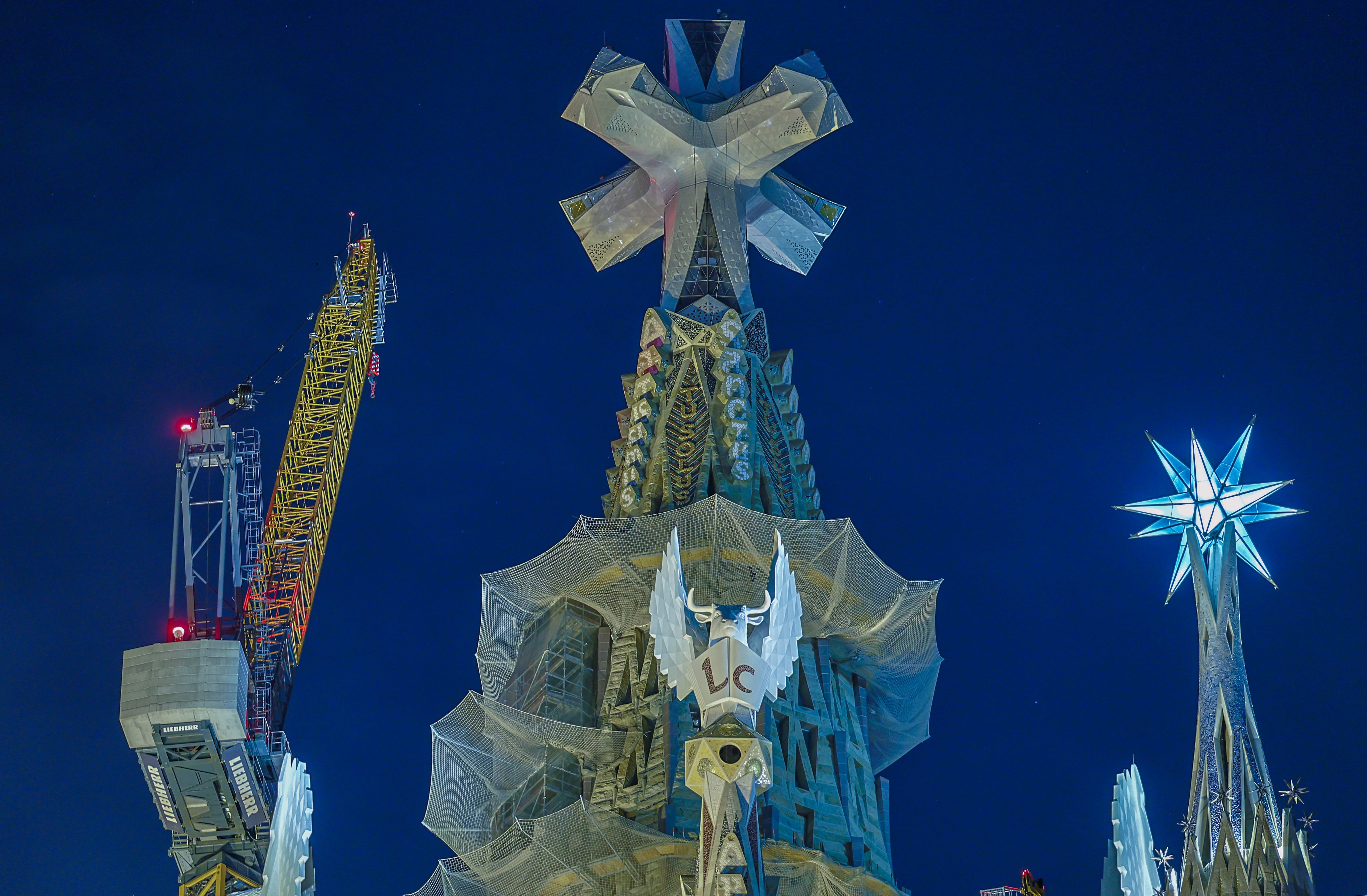 La torre de Jesucristo de la Sagrada Familia, en el centro, y coronada por la estrella. En primer plano, la torre del evangelista Lucas; y a la izquierda, la torre de María, con la estrella iluminada.
