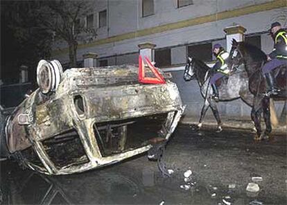 Dos policías a caballo pasan junto al coche incendiado cerca del campo bético.