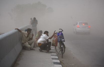 Viajeros indios tratan de protegerse en la cuneta de una carretera durante una fuerte tormenta de polvo en Jammu, India.