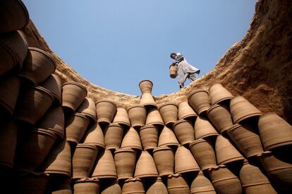 Un hombre porta una maceta de barro para colocarla junto a otras dentro de un horno en una fábrica improvisada de Peshawar (Pakistán).